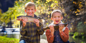 Two laughing young boys each holding up a caught bass for the camera.